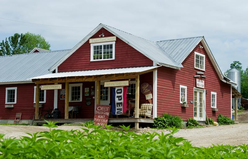 A red barn seen from outside with an Open flag and a sign reading “Taylor Farm Cheese.”