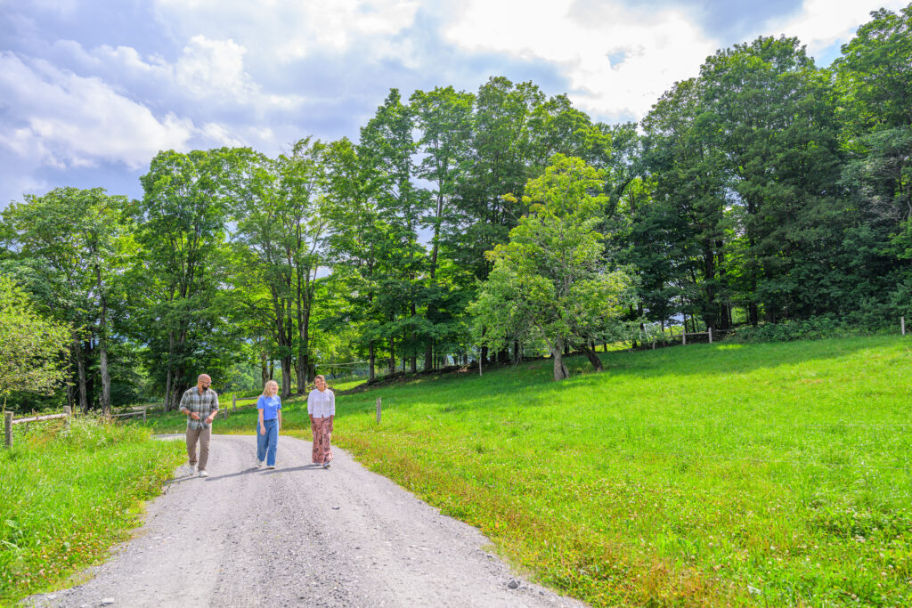 Three people walk toward the camera on a gravel path through a green field in the summer.