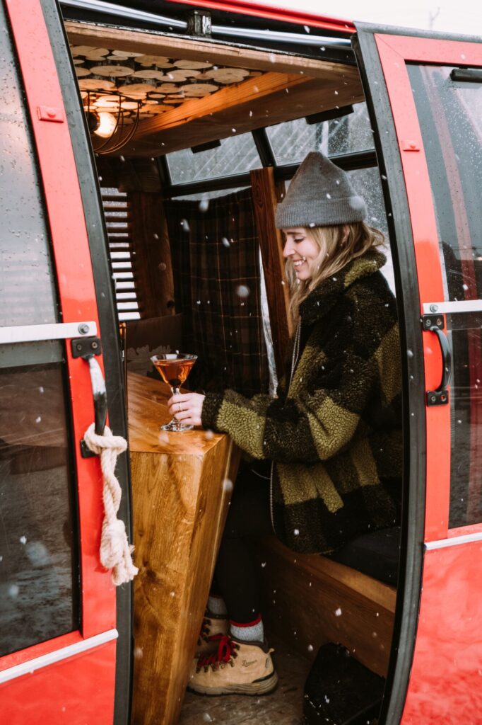 People inside a repurposed ski gondola with a wooden table having cocktails.