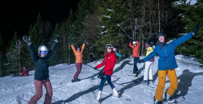 A group of people on skis look toward a camera and smile.