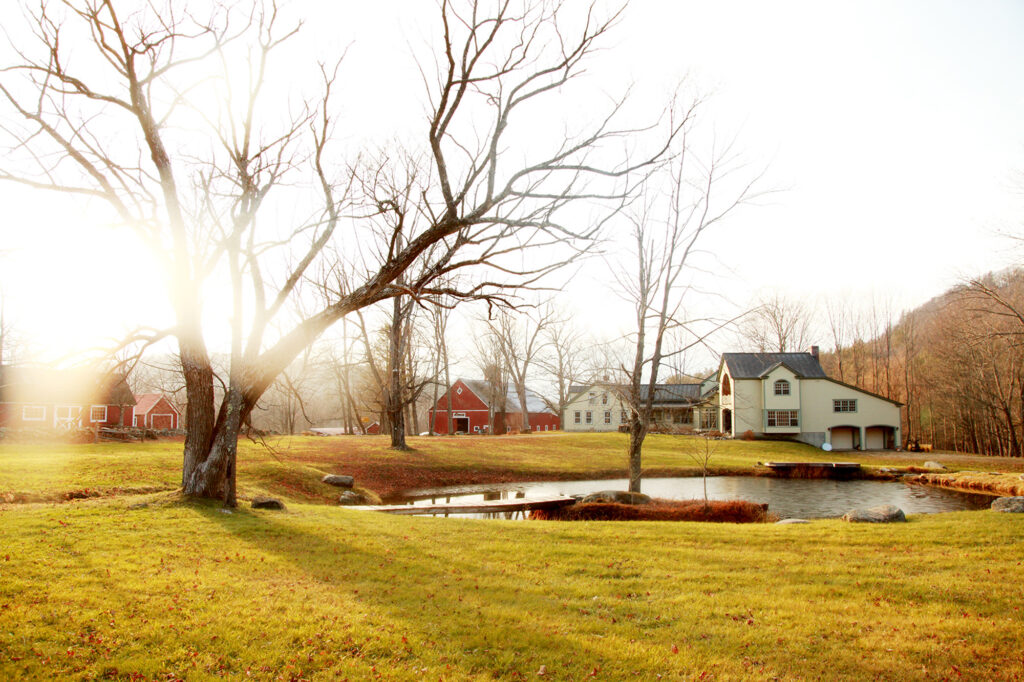 Mist rises at a farm photographed outdoors with a white farmhouse and a red barn.