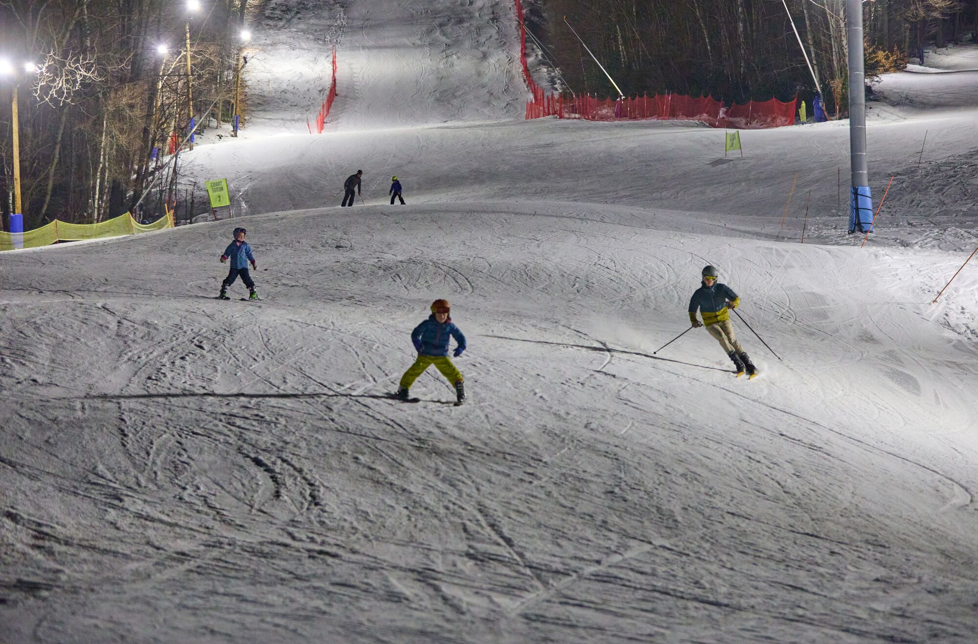 Skiers of various ages come down a snowy trail in winter at a ski resort.